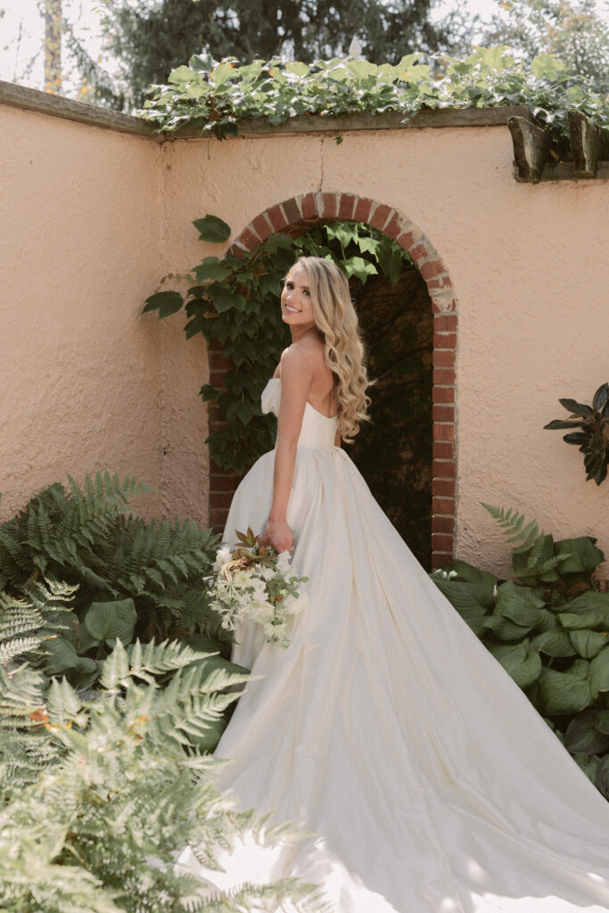 Bride poses in front of archway with her gown and bouquet