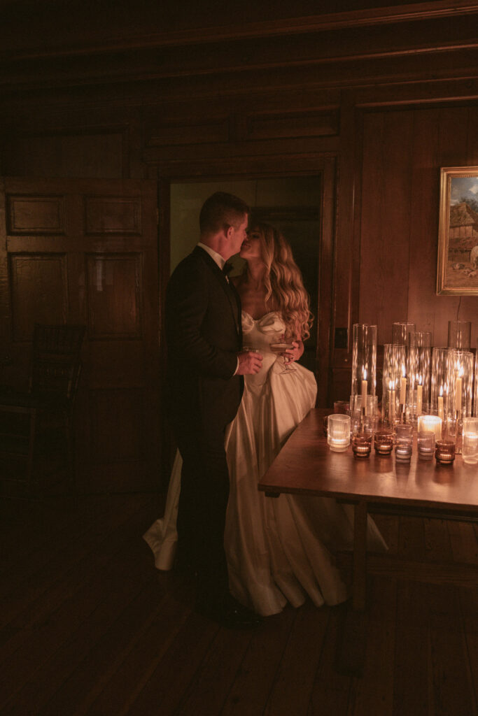 Bride and groom share a kiss in a candlelit room during their reception