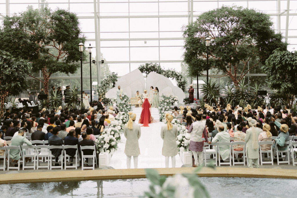Wide view of a South Asian wedding ceremony at the Gaylord National Resort with a white floral mandap and guests filling the atrium.