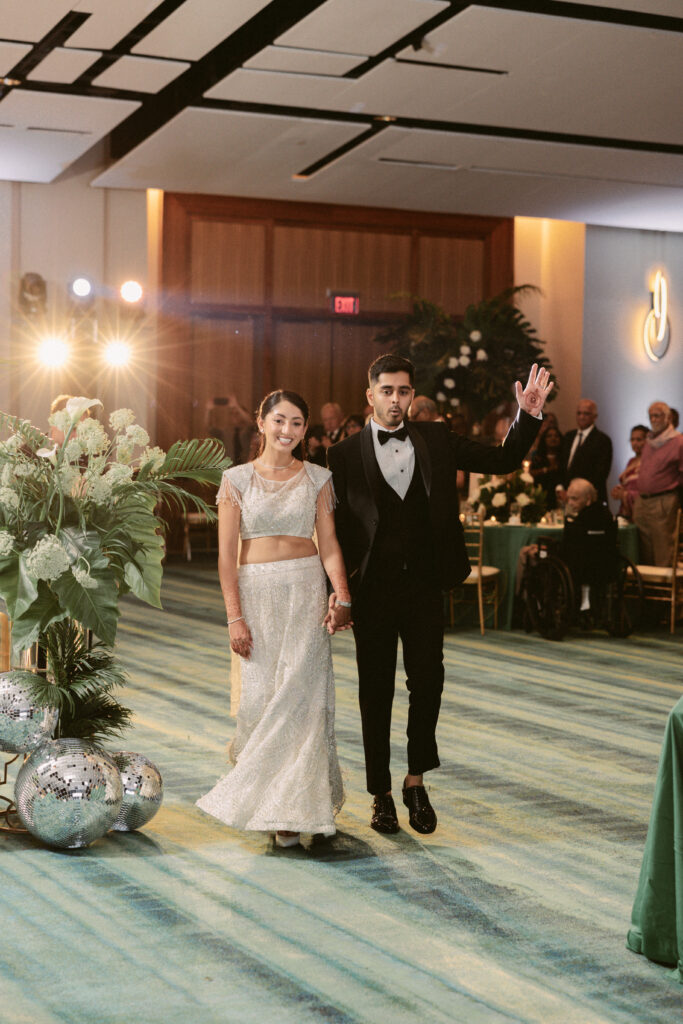 Bride and groom make a grand entrance into their South Asian wedding reception at the Gaylord National Resort, smiling and holding hands.