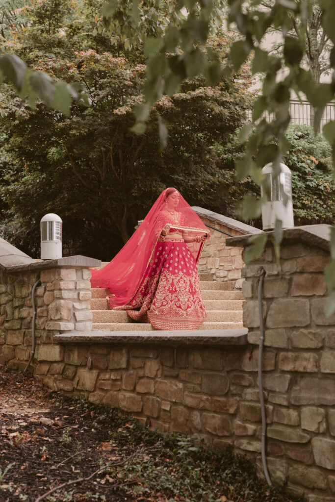 South Asian bride walks down steps to her first look with her red dupatta cascading behind her
