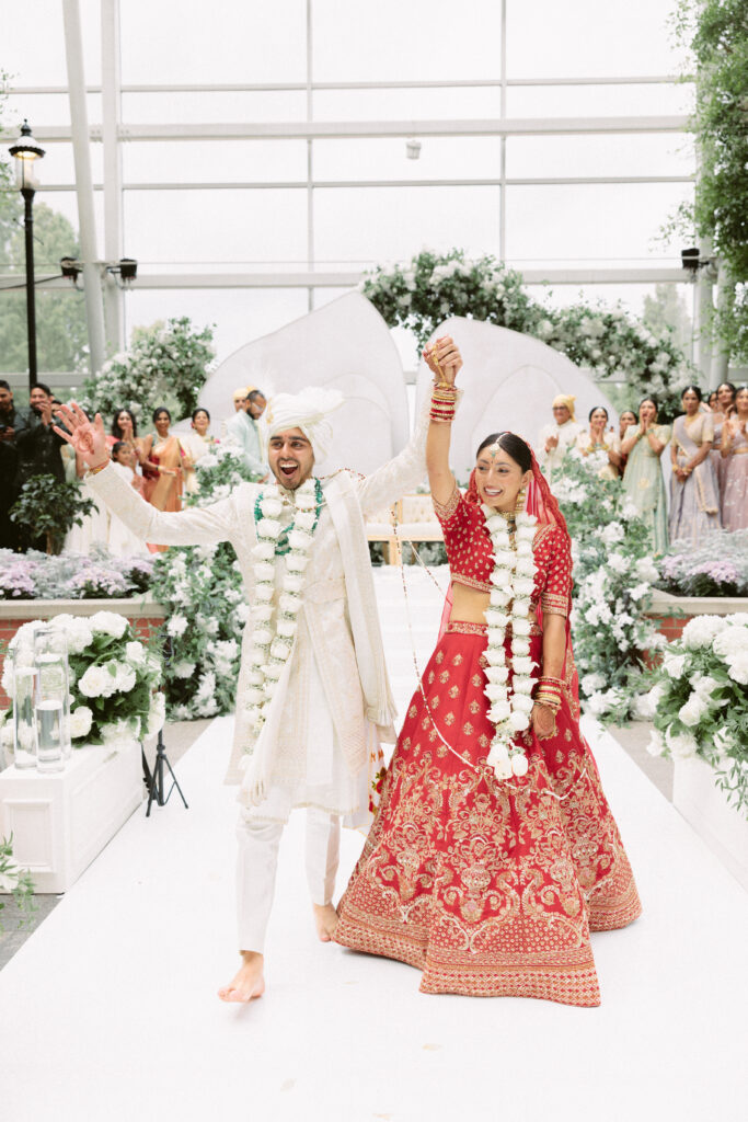 Newly married South Asian couple walks joyfully down the aisle, holding hands and smiling during their Gaylord National Resort wedding.