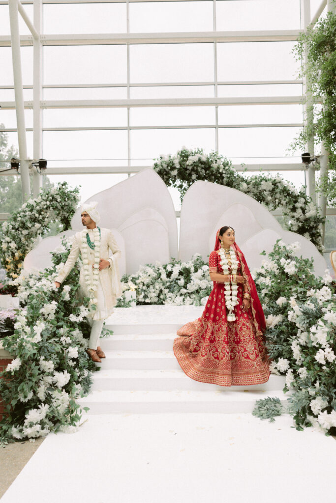 Bride and groom holding hands on the white floral mandap steps during their South Asian wedding ceremony at the Gaylord National Resort.