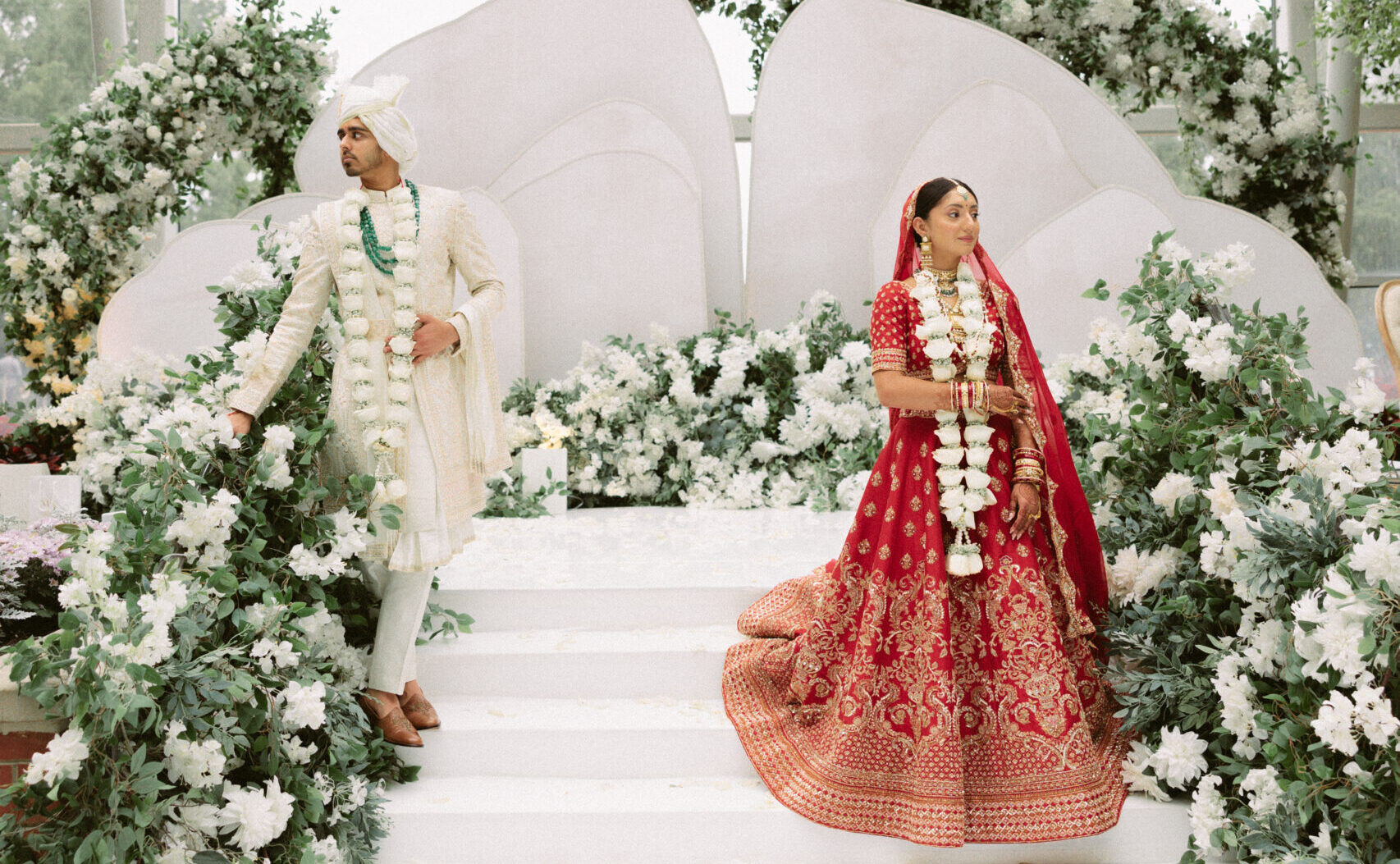 Bride and groom holding hands on the white floral mandap steps during their South Asian wedding ceremony at the Gaylord National Resort.