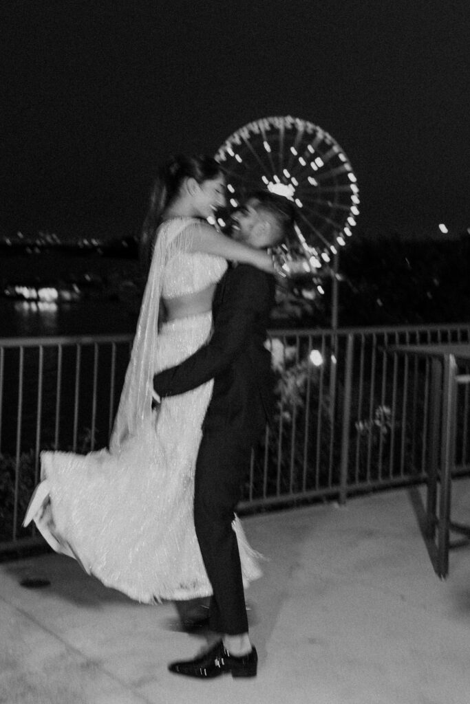 Romantic nighttime portrait of the bride and groom dancing with the National Harbor Ferris wheel glowing behind them.