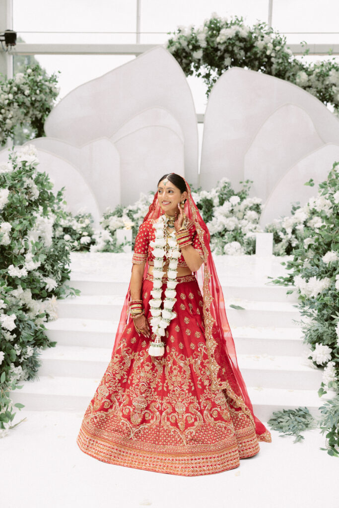 South Asian bride poses in her stunning red lehenga in front of the mandap