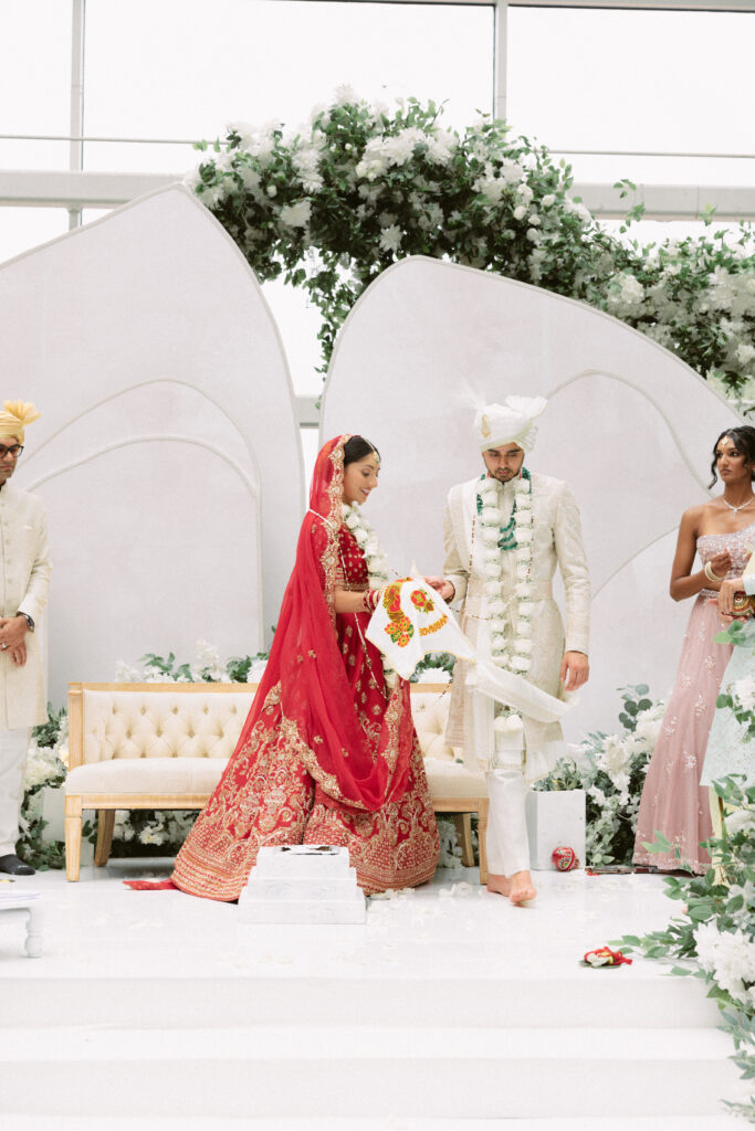 Bride and groom holding hands on the white floral mandap steps during their South Asian wedding ceremony at the Gaylord National Resort.